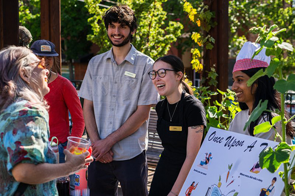 Students stand behind a table talking with a visitor