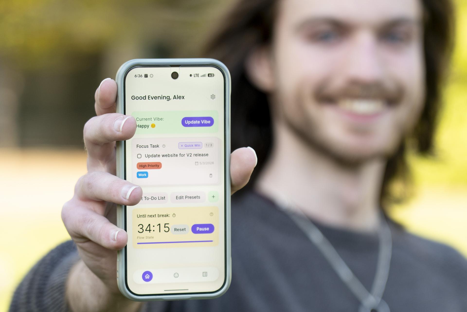 Alex Hines holds up a phone showing his app, VibeCheckList