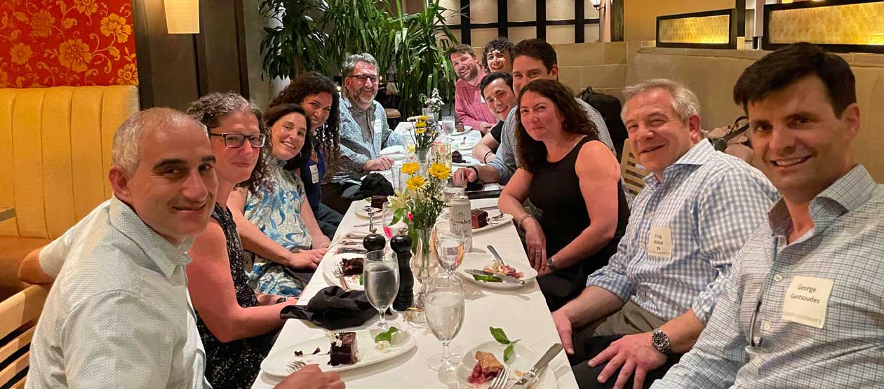 Group of ten alumni gathering in a vibrantly colored restaurant around a long rectangular table.