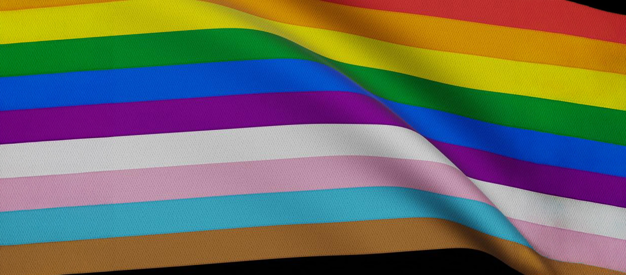 a pride flag with a rainbox of colors is seen as if waving in the breeze