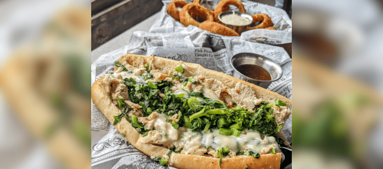 a cheesesteak and onion rings are pictured with a sauce on the side