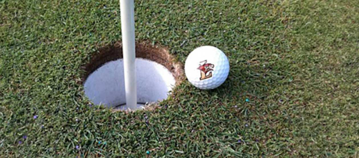 a Lehigh branded golf ball rests next to the hole on a golf green