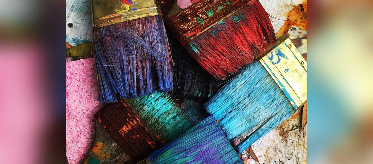 paint brushes, filled with paint, are arranced on a studio work space
