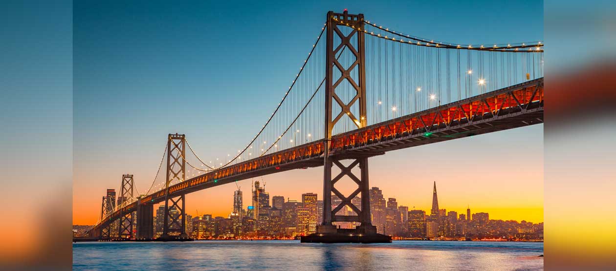 The Golden Gate Bridge in the foreground, with the bay below and the San Francisco skyline in the background at sunset The Golden Gate Bridge in the foreground, with the bay below and the San Francisco skyline in the background at sunset