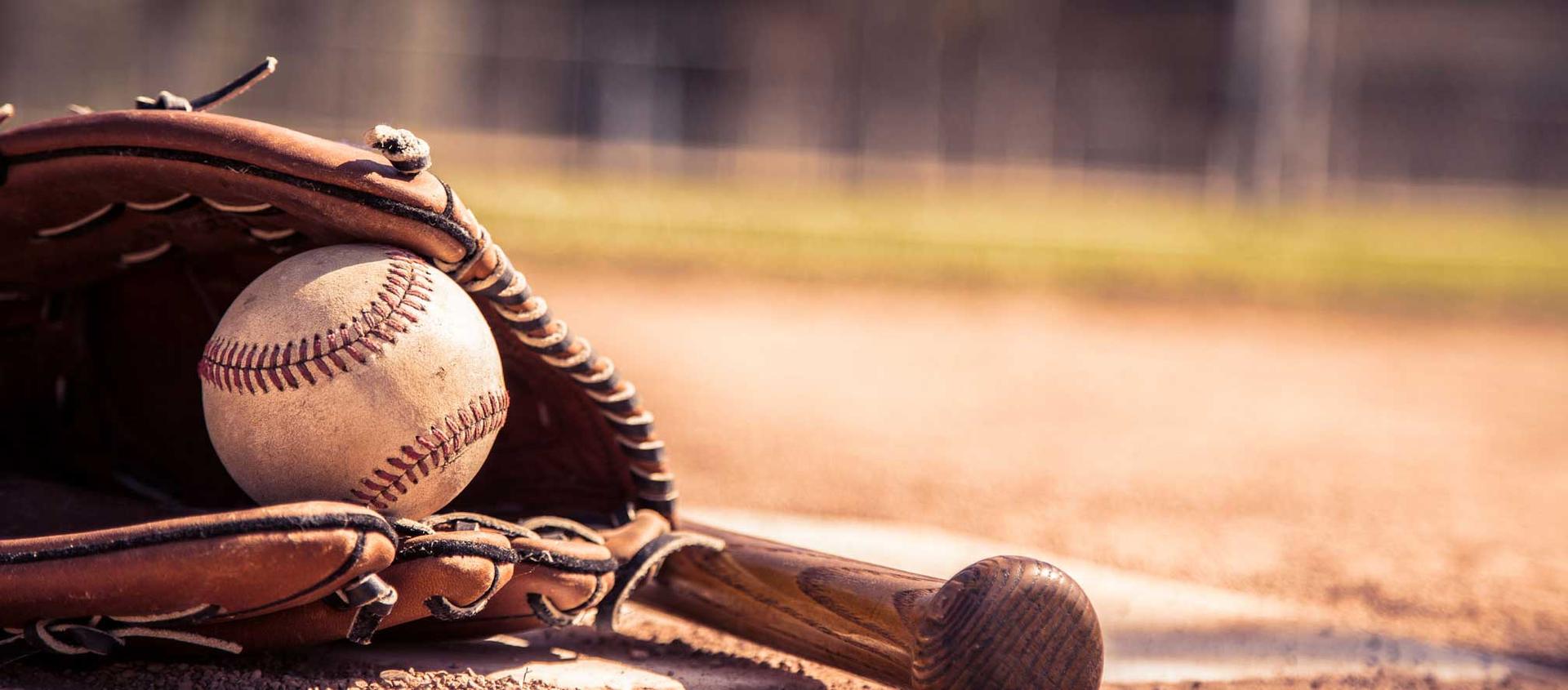 a baseball rests in a mitt, with a bat laying next to it, on a base mound