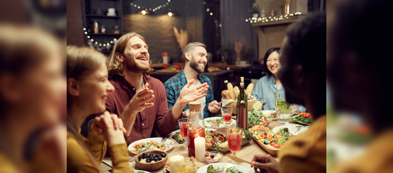 people gathered around a table with food and drink, laughing people gathered around a table with food and drink, laughing