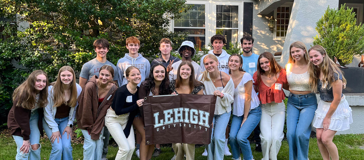 Incoming students posing with a brown Lehigh University flag at a Boston Student Sendoff